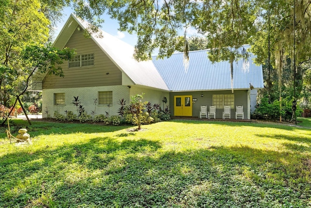 rear view of house featuring a yard, metal roof, and brick siding