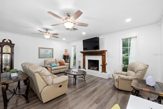 living room with recessed lighting, visible vents, ornamental molding, a brick fireplace, and wood finished floors