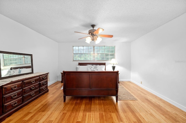 bedroom featuring baseboards, ceiling fan, light wood-style flooring, and a textured ceiling