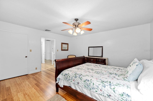 bedroom featuring light wood finished floors, a textured ceiling, visible vents, and a ceiling fan