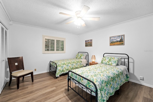 bedroom with a closet, ornamental molding, a textured ceiling, wood finished floors, and baseboards