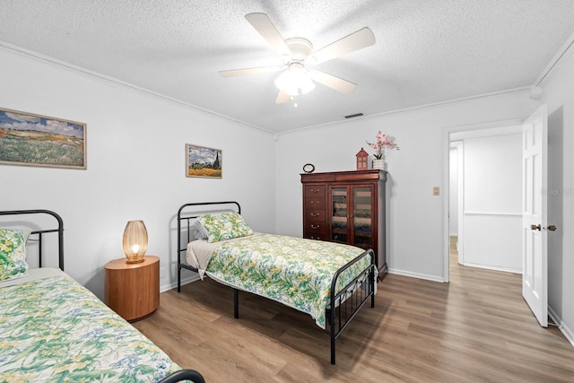 bedroom with crown molding, a textured ceiling, visible vents, and wood finished floors