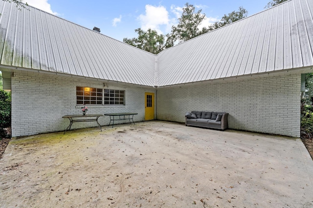 rear view of house featuring metal roof, a patio, brick siding, and a chimney