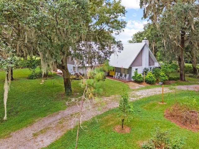 view of front of house with dirt driveway, metal roof, a front lawn, and a chimney