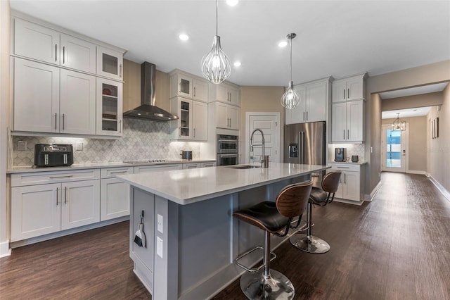 kitchen with a center island with sink, dark wood-type flooring, stainless steel appliances, wall chimney range hood, and a sink