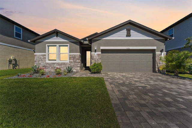 view of front of home featuring an attached garage, stone siding, decorative driveway, stucco siding, and a front yard