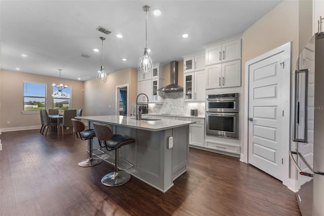 kitchen with visible vents, decorative backsplash, appliances with stainless steel finishes, a sink, and wall chimney range hood