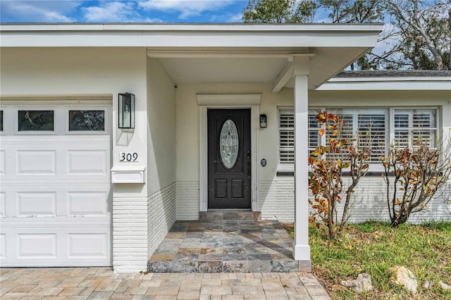 view of exterior entry with a garage, brick siding, and stucco siding