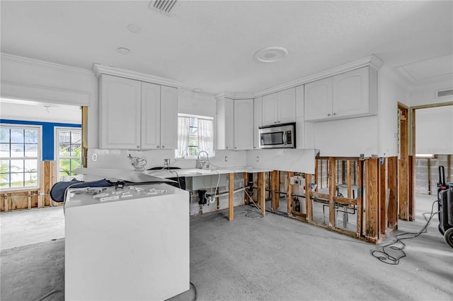 kitchen with concrete flooring, white cabinets, stainless steel microwave, and visible vents