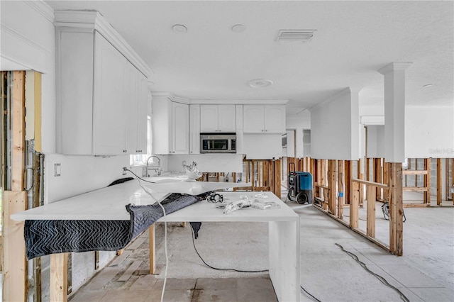 kitchen with light countertops, stainless steel microwave, visible vents, white cabinetry, and a sink