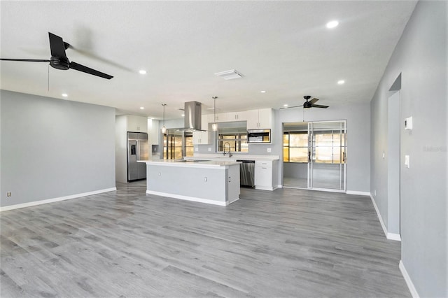 kitchen featuring white cabinets, a kitchen island, appliances with stainless steel finishes, open floor plan, and light countertops