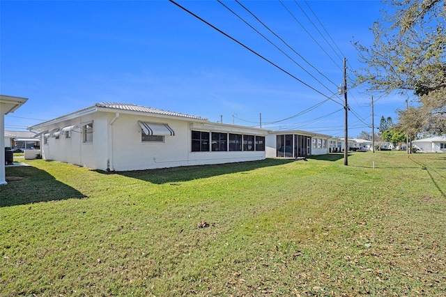 back of property with a sunroom, a tile roof, a lawn, and stucco siding