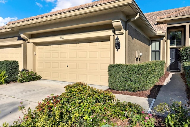 exterior space featuring a tile roof, an attached garage, driveway, and stucco siding