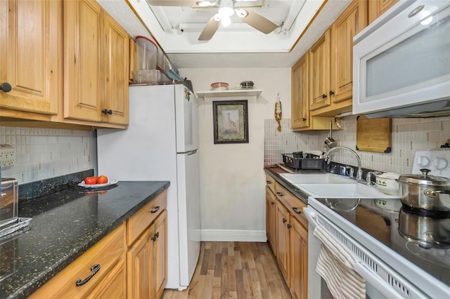 kitchen with a tray ceiling, light wood-style flooring, backsplash, a ceiling fan, and white appliances