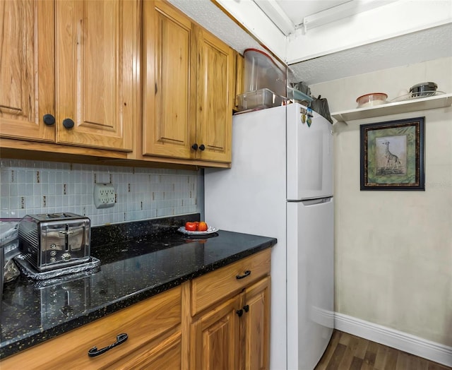 kitchen with tasteful backsplash, freestanding refrigerator, brown cabinets, and baseboards