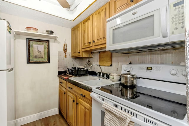 kitchen with white appliances, a sink, baseboards, decorative backsplash, and light wood finished floors