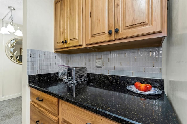 kitchen featuring hanging light fixtures, dark stone countertops, baseboards, and backsplash