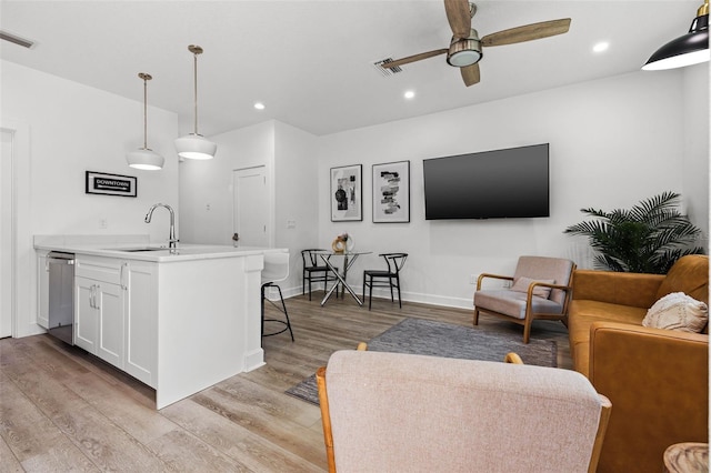 interior space with ceiling fan, a sink, visible vents, white cabinets, and light wood finished floors