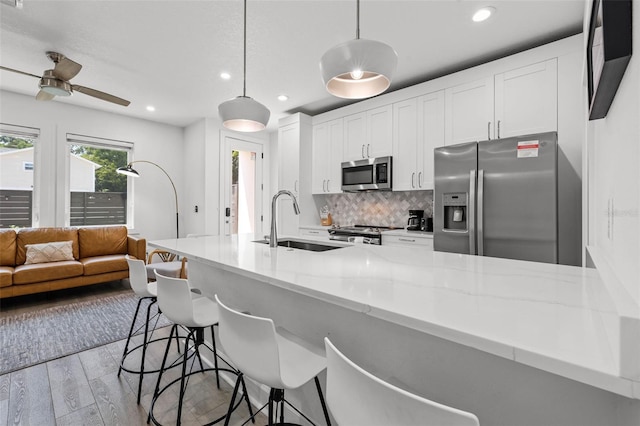 kitchen featuring stainless steel appliances, decorative backsplash, white cabinets, a sink, and wood finished floors