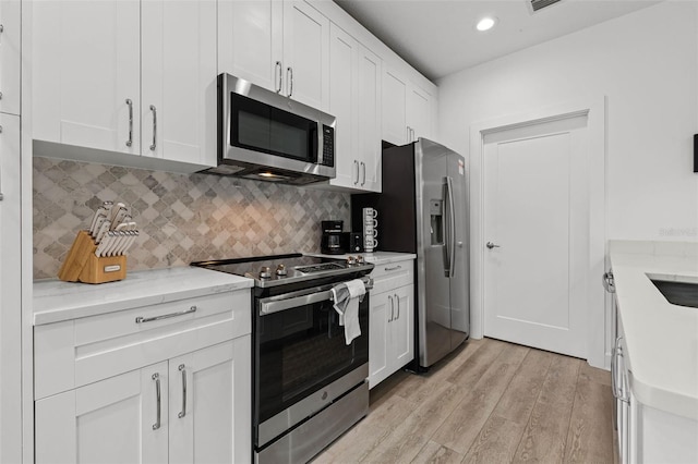 kitchen featuring stainless steel appliances, recessed lighting, backsplash, light wood-style flooring, and white cabinets