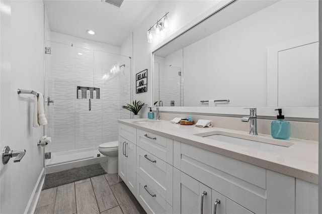 bathroom with double vanity, toilet, a stall shower, wood tiled floor, and a sink