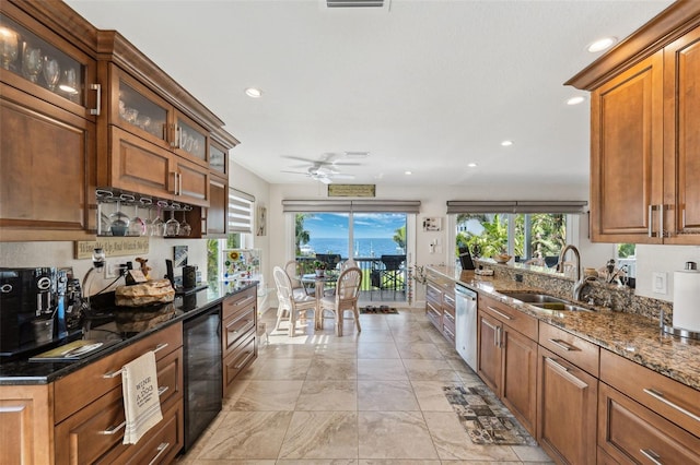 kitchen featuring wine cooler, a sink, brown cabinets, dark stone countertops, and glass insert cabinets