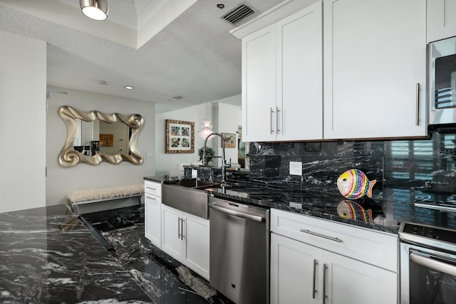 kitchen with dark stone countertops, a sink, stainless steel appliances, white cabinetry, and backsplash