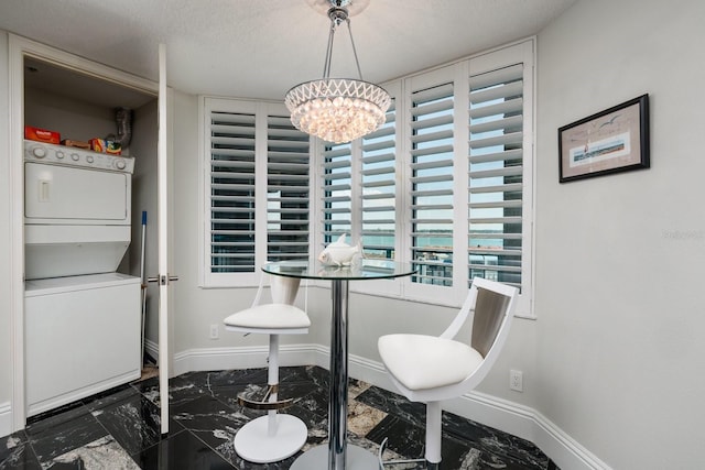 dining room with marble finish floor, baseboards, a textured ceiling, and stacked washer and clothes dryer