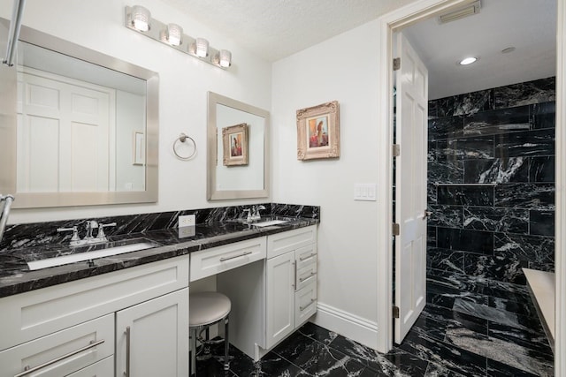 bathroom with marble finish floor, double vanity, a tile shower, and visible vents