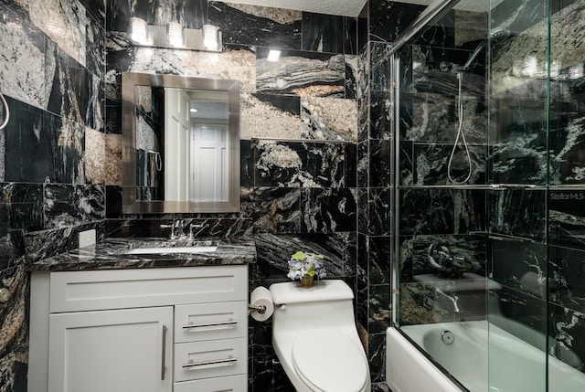 bathroom featuring toilet, bath / shower combo with glass door, tile walls, and vanity