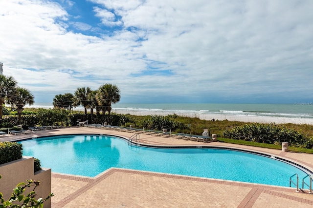 pool featuring a beach view, a patio area, and a water view