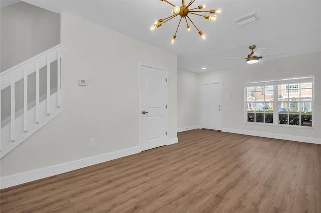 unfurnished room with ceiling fan with notable chandelier, visible vents, baseboards, and wood finished floors