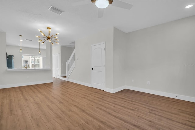 unfurnished living room with visible vents, stairway, wood finished floors, baseboards, and ceiling fan with notable chandelier