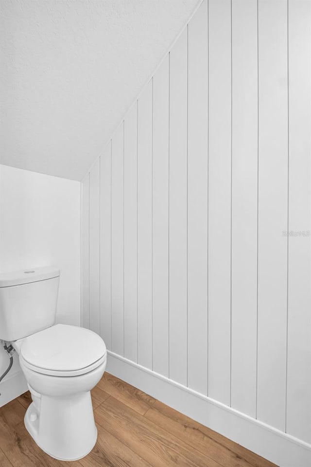 bathroom featuring toilet, wood finished floors, and lofted ceiling