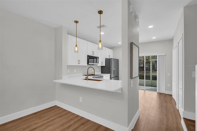 kitchen featuring baseboards, visible vents, wood finished floors, stainless steel appliances, and light countertops