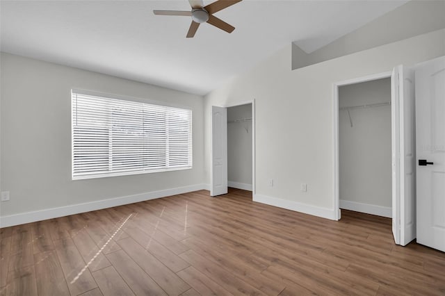 unfurnished bedroom with lofted ceiling, wood finished floors, a ceiling fan, baseboards, and two closets