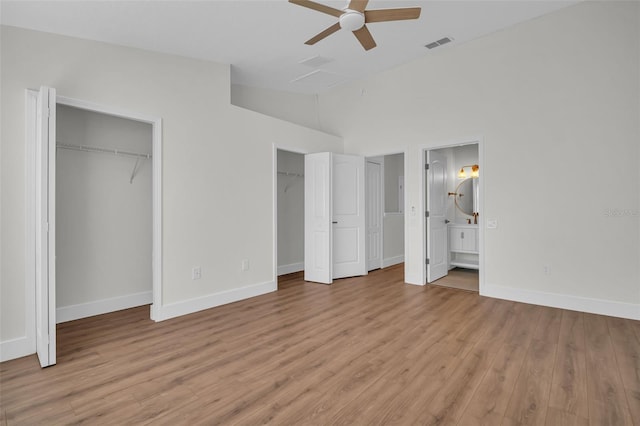 unfurnished bedroom with light wood finished floors, baseboards, lofted ceiling, ensuite bathroom, and multiple closets