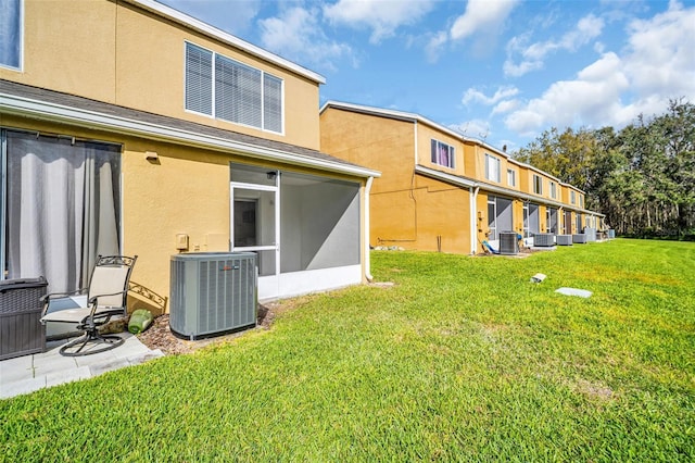 rear view of property with central air condition unit, a sunroom, a lawn, and stucco siding