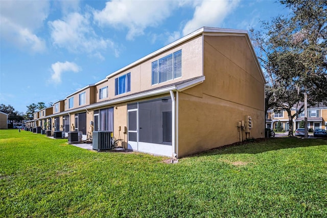 rear view of house with central AC unit, a lawn, and stucco siding