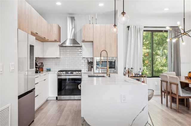 kitchen featuring stainless steel appliances, modern cabinets, light wood-style flooring, wall chimney range hood, and light stone countertops