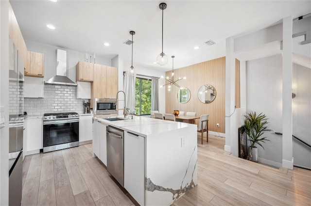 kitchen featuring stainless steel appliances, a sink, wall chimney range hood, light wood-type flooring, and modern cabinets