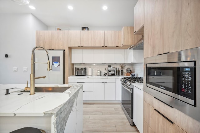 kitchen featuring range with gas stovetop, stainless steel microwave, backsplash, light brown cabinets, and a sink