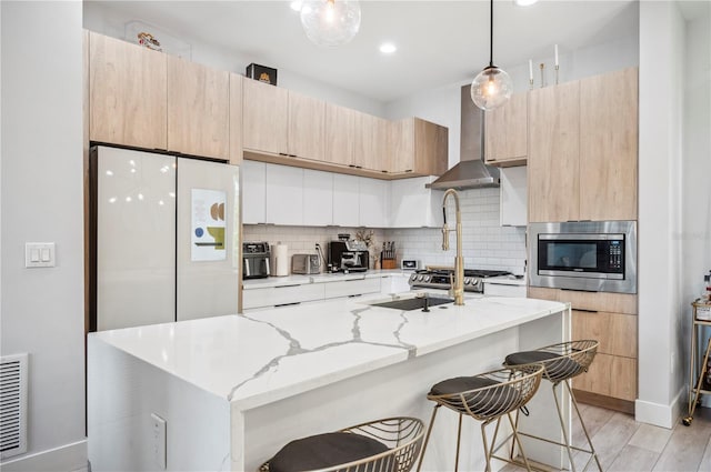 kitchen with light stone counters, wall chimney range hood, backsplash, stainless steel microwave, and modern cabinets