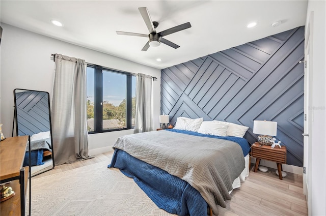 bedroom with ceiling fan, an accent wall, light wood-style flooring, and baseboards