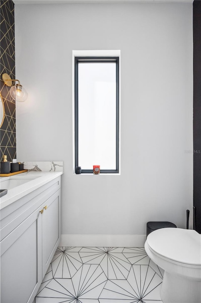 half bath with tile patterned flooring, baseboards, vanity, and toilet