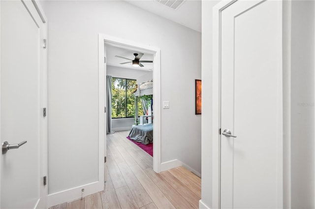 corridor with baseboards, visible vents, and light wood finished floors