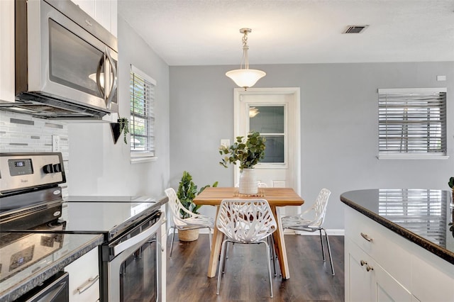 kitchen with visible vents, dark wood-style floors, stainless steel appliances, white cabinetry, and backsplash