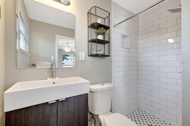 full bath with a tile shower, vanity, toilet, and ceiling fan