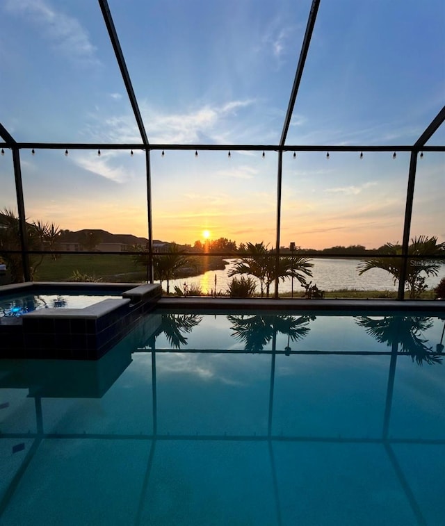 pool at dusk with glass enclosure, a patio area, and a pool with connected hot tub