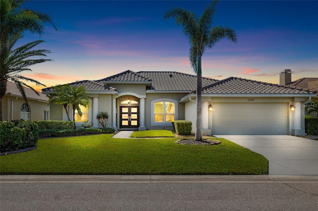 mediterranean / spanish-style house featuring stucco siding, a lawn, driveway, a garage, and a tiled roof